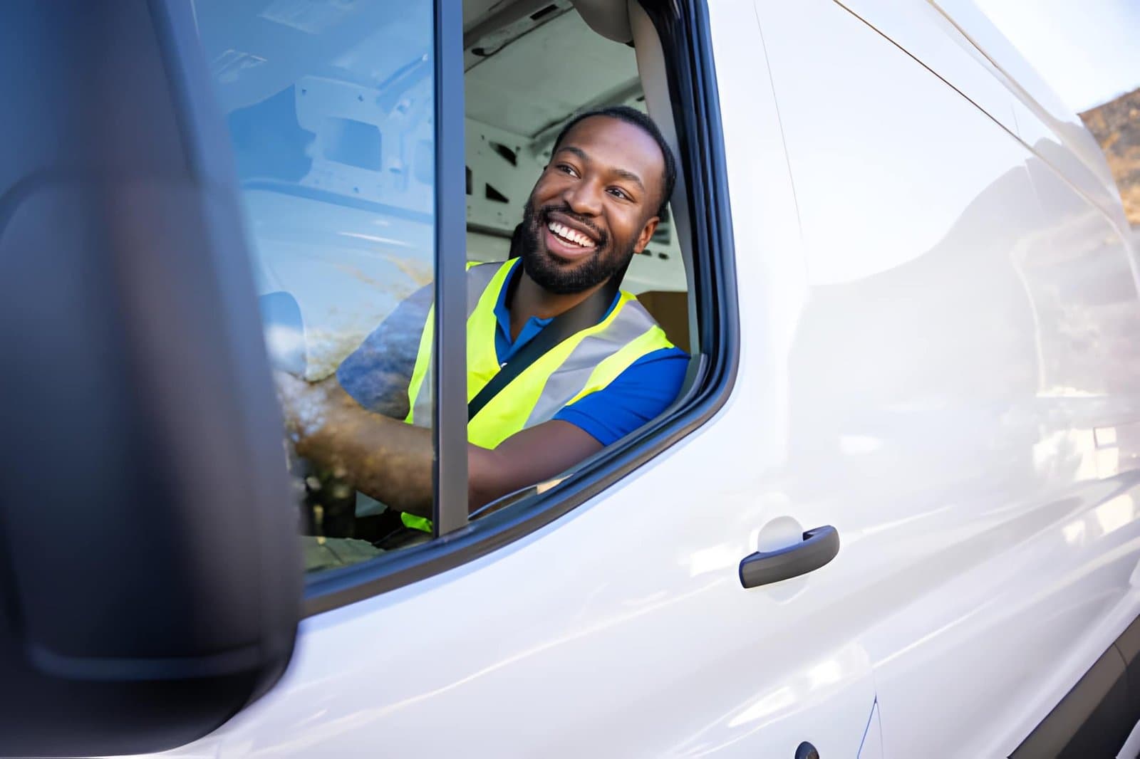 A smiling delivery driver in a hi-vis vest leaning out of a white van window