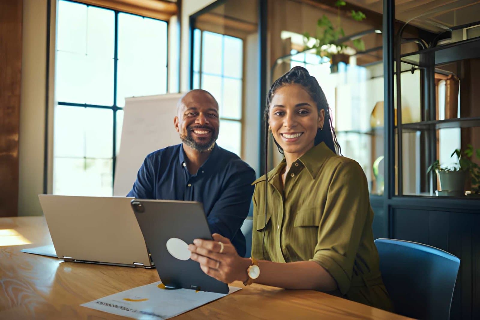 Two smiling business professionals reviewing work on a tablet in an office