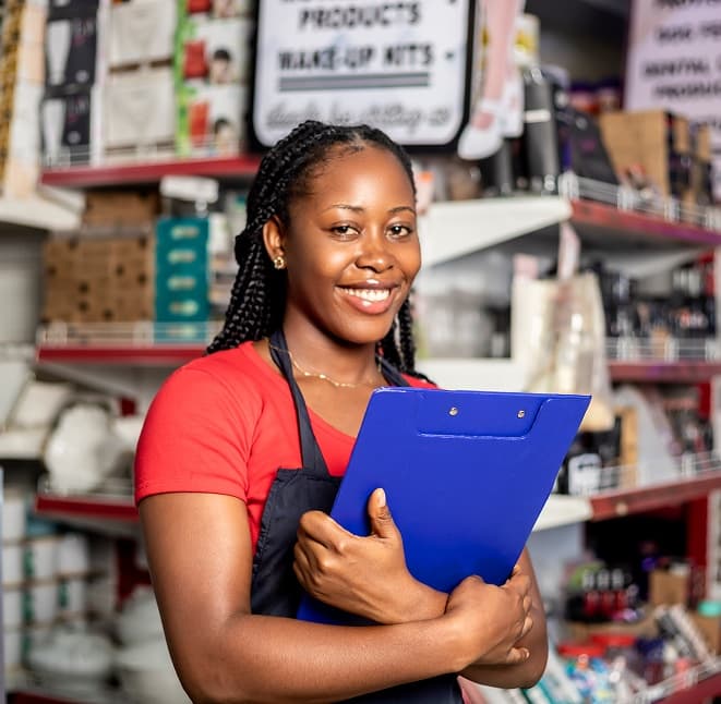 A smiling retail worker in an apron holding a clipboard in a store