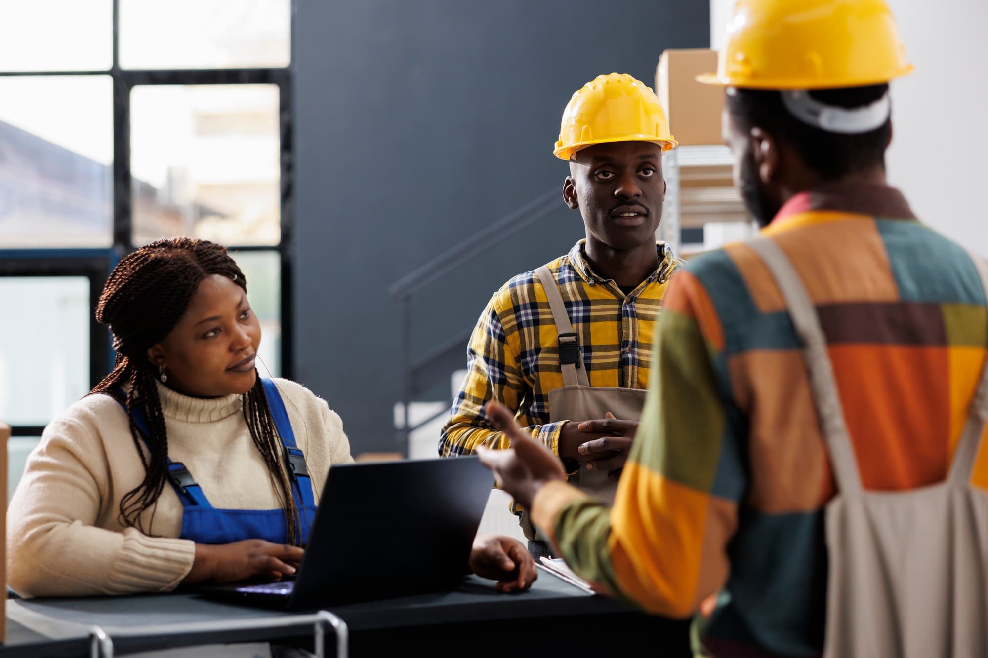 Factory workers in hard hats reviewing production on a laptop