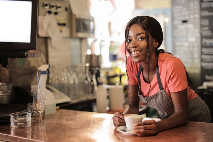 A smiling barista leaning on the counter of a cafe